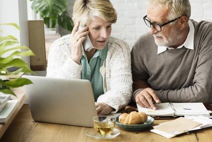 Älteres Ehepaar arbeitet mit Notebook, Ringbuch und Telefon