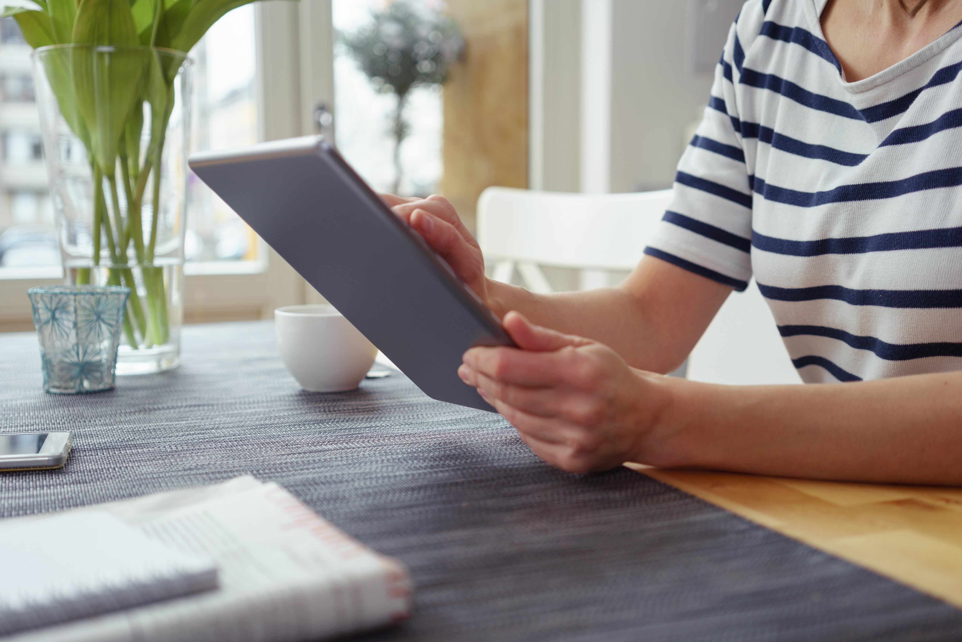 Frau sitzt am Tisch und tippt in ein Tablet