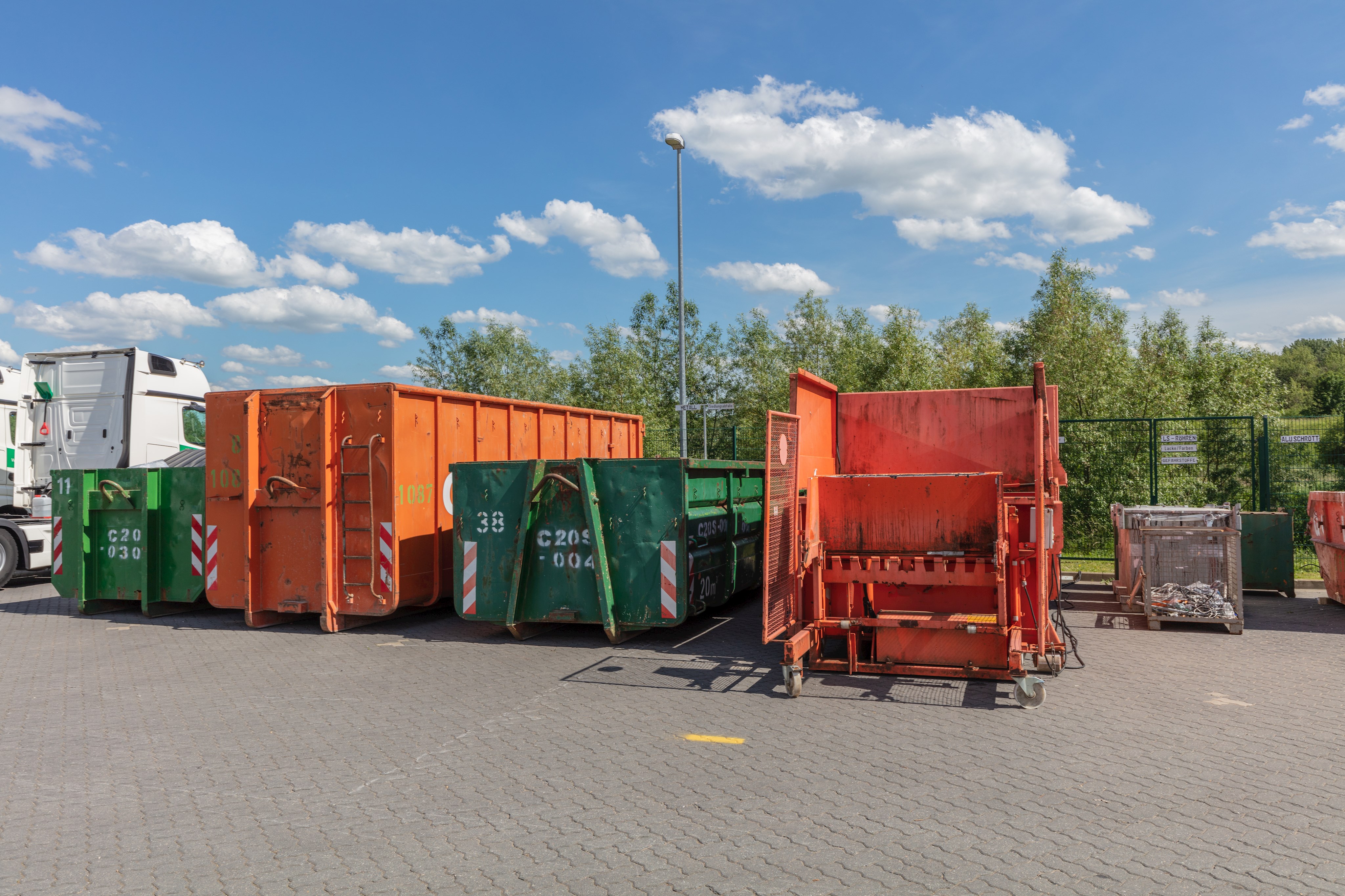 Orangefarbene Müllpresse, daneben große Müllcontainer