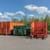 Orangefarbene Müllpresse, daneben große Müllcontainer