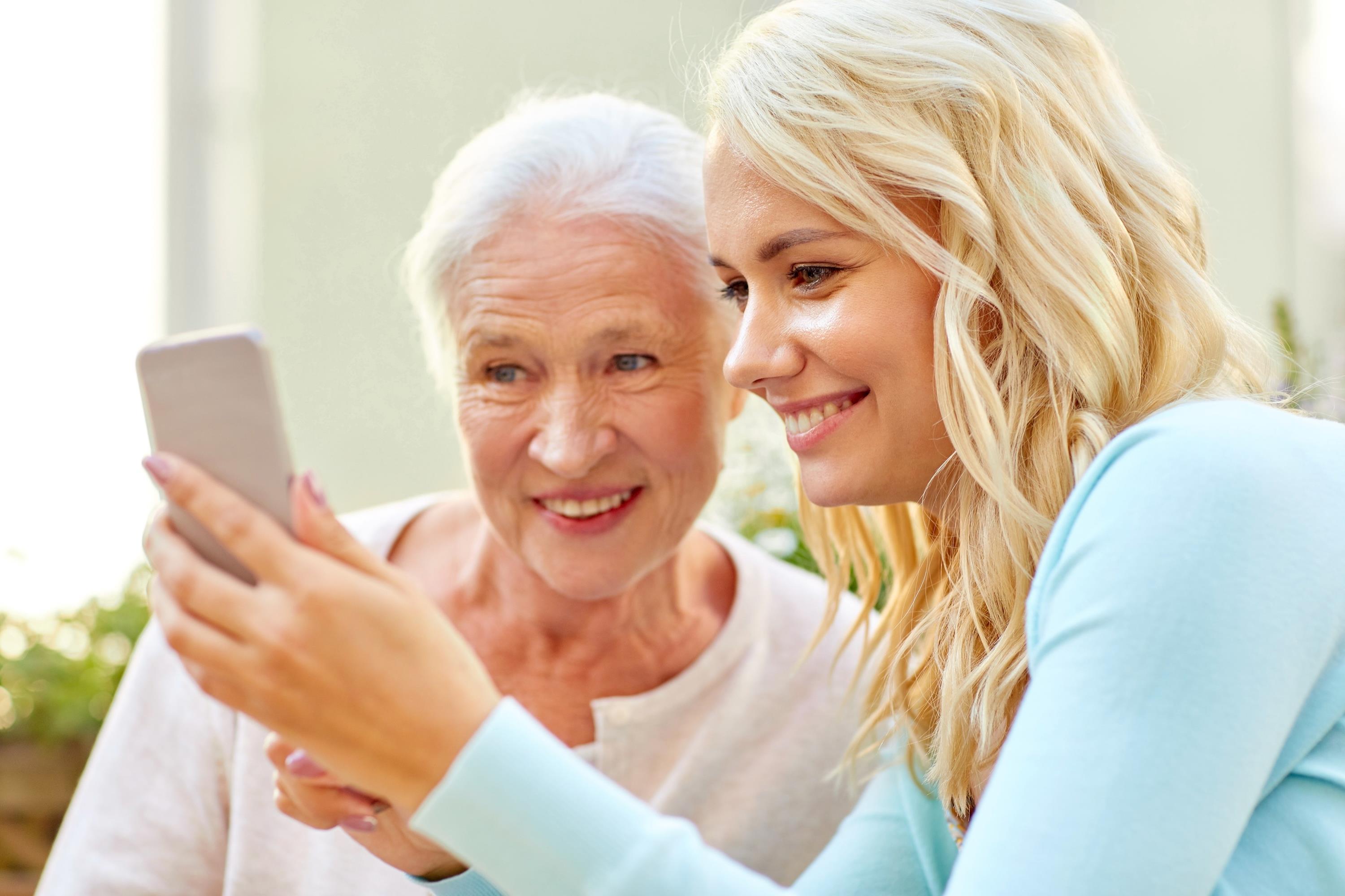 glücklich lächelnde junge Tochter und ältere Mutter mit Smartphone